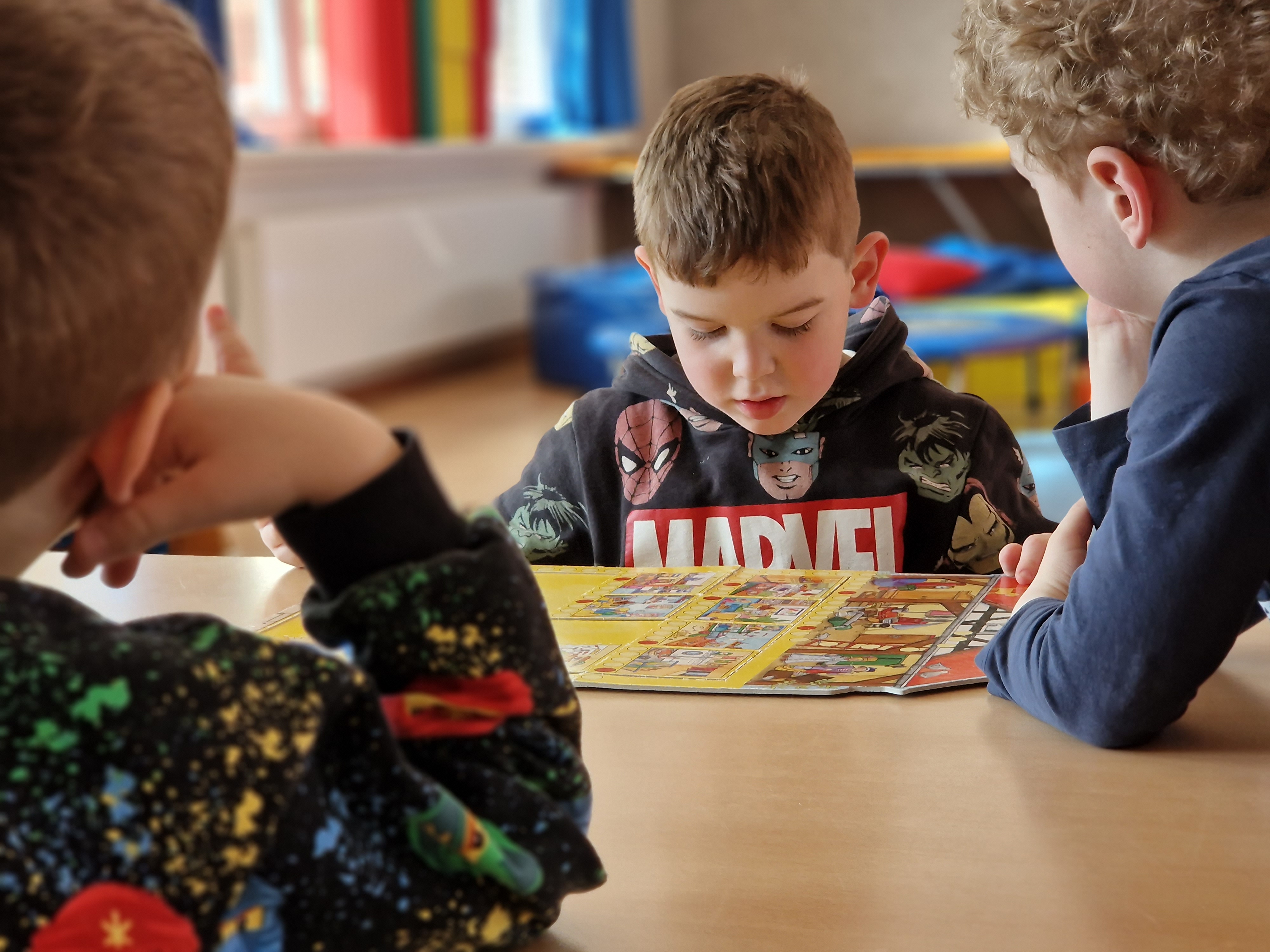 Drei Kleinkinder beugen sich über ein Brettspiel.
