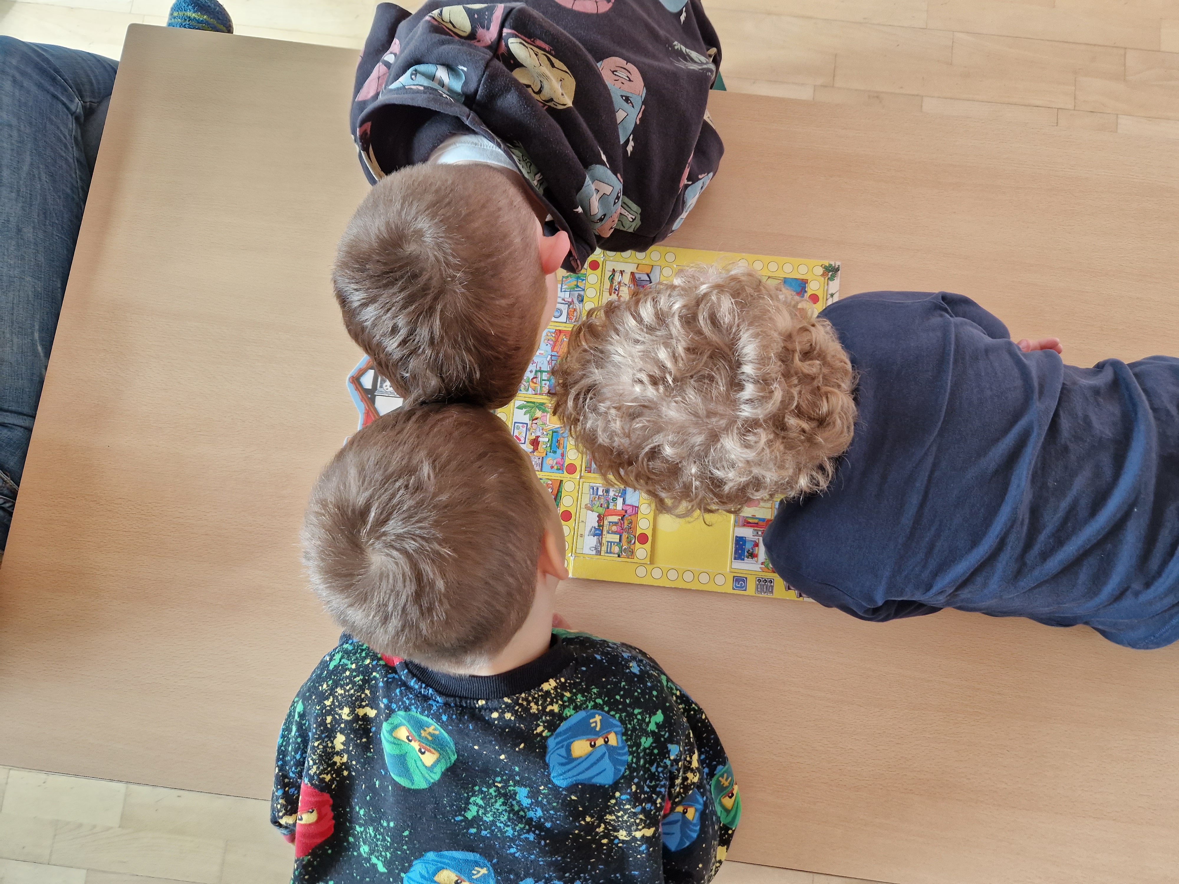 Drei Kinder beugen sich über ein Brettspiel.