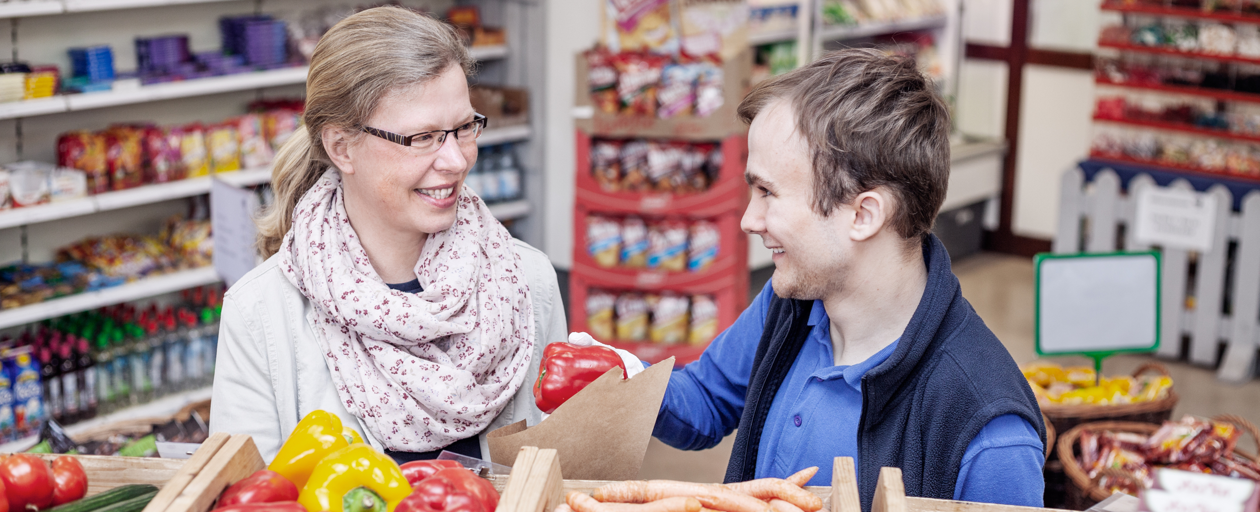 Eine Frau und ein junger Mann in einem Laden vor einer Gemüse-Auslage