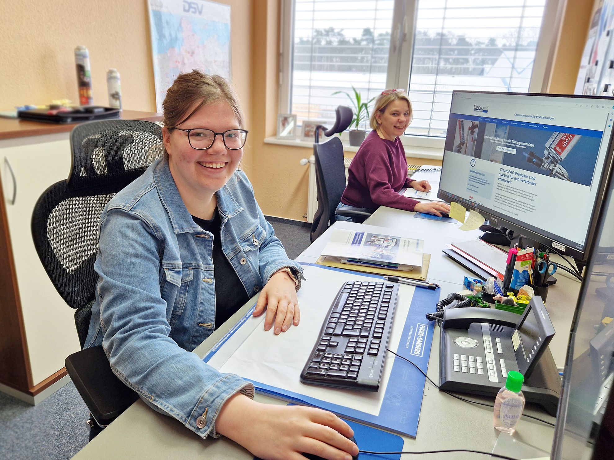 Zwei Frauen sitzen in einem Büro an ihrem jeweiligen Schreibtisch mit Computer.