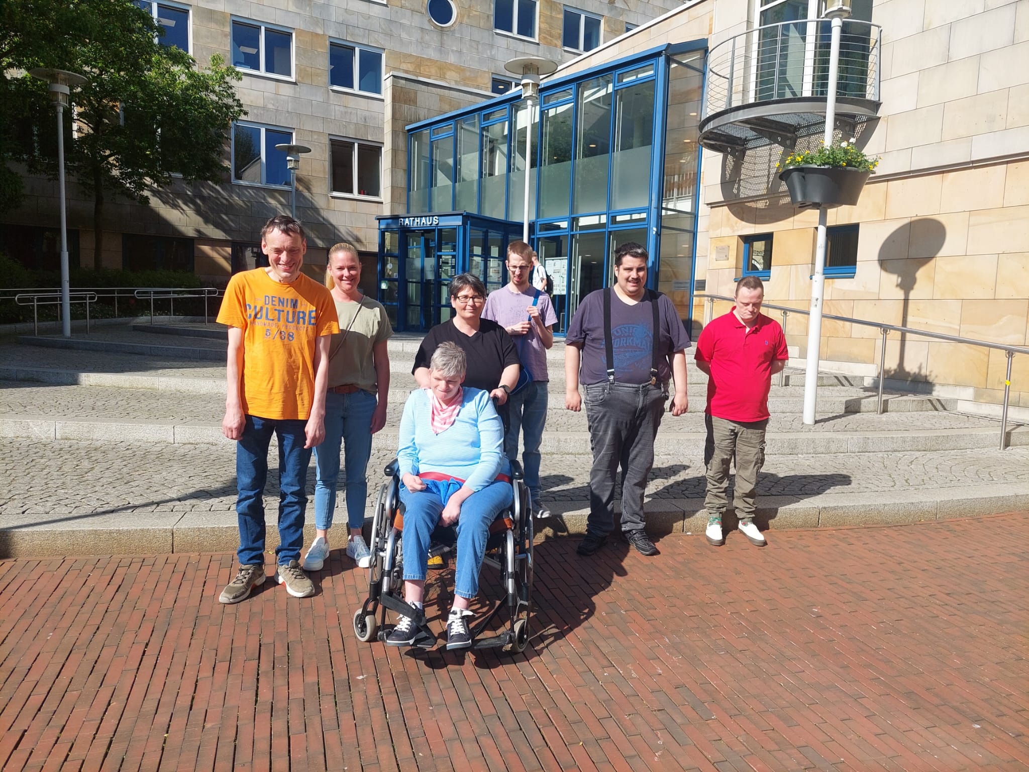 Sieben Menschen, eine Person ist in einem Rollstuhl, stehen vor dem Rathaus der Stadt Lingen. 
