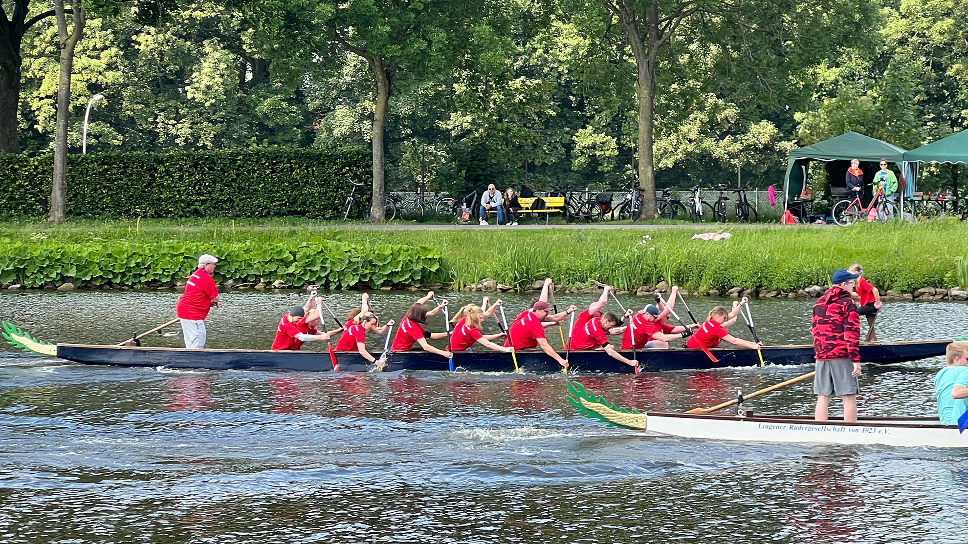 Mehrere Menschen mit roten Shirts sitzen in einem Boot und tauchen die Paddel in Wasser.