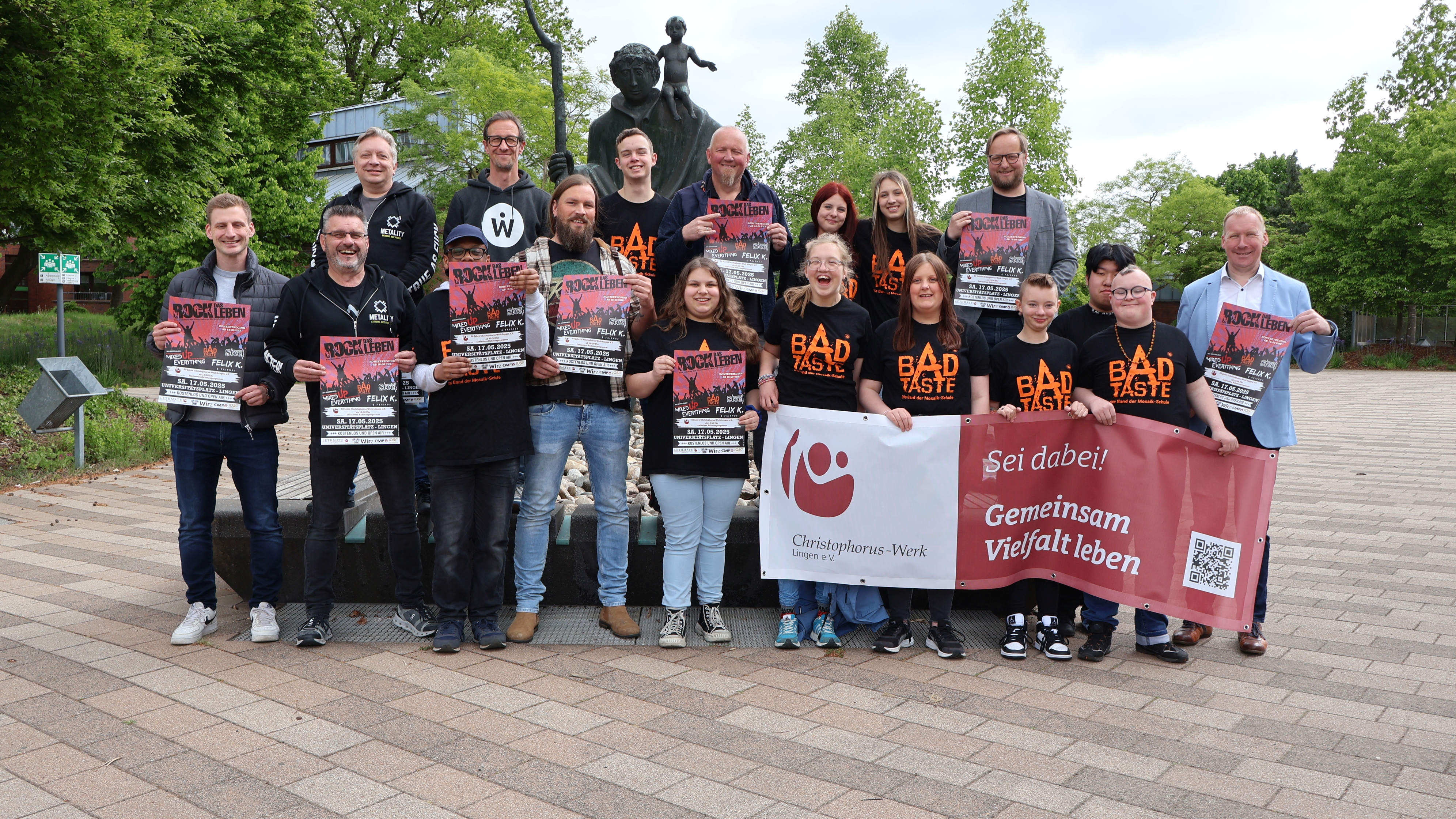 Menschen stehen vor einer Statue des heiligen Christophorus. Kinder halten ein Banner mit der Aufschrift 