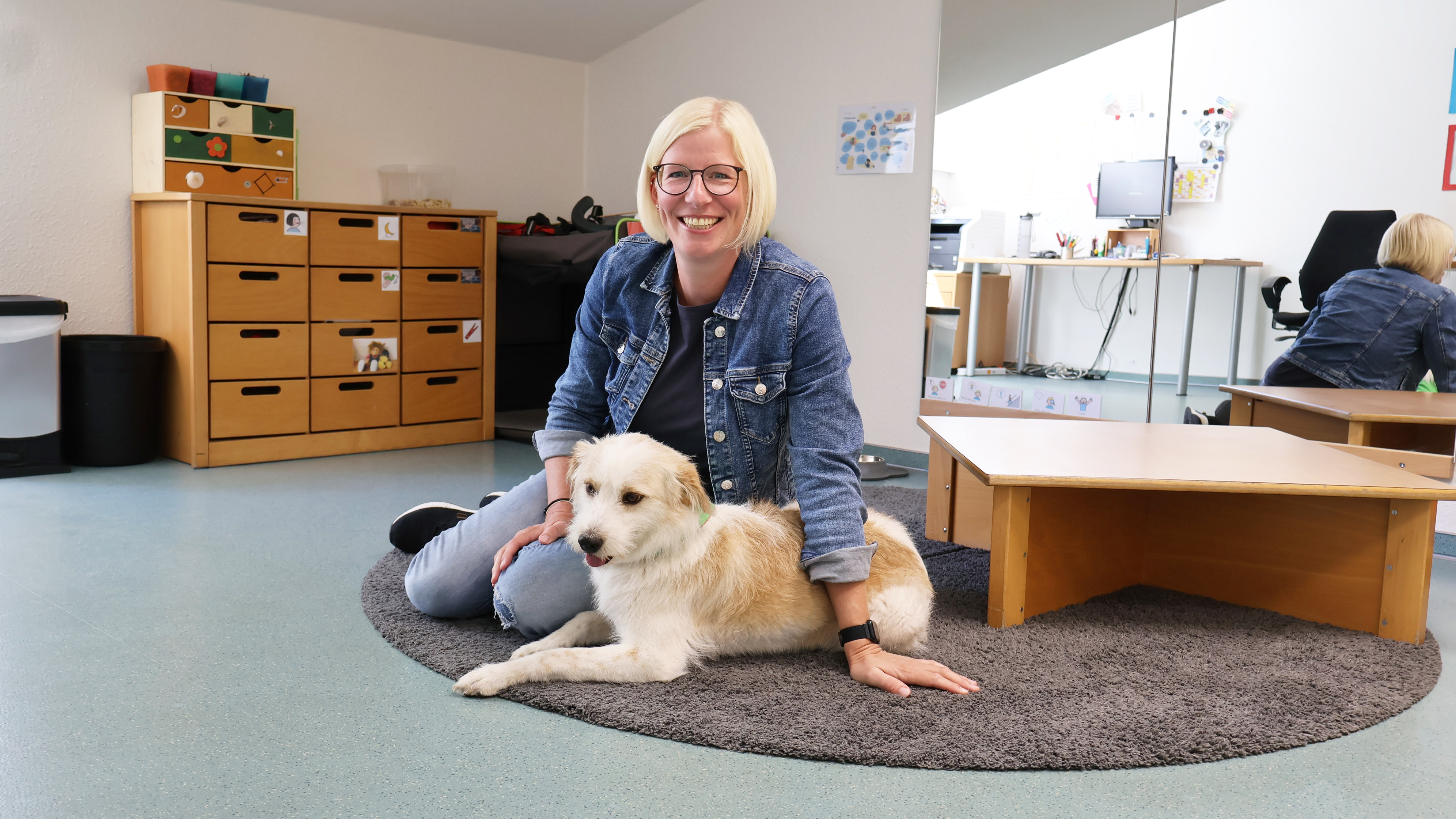 Logop&auml;din Christiane Kr&auml;mer und ihr Hund Alma sitzen gemeinsam auf dem Boden in ihrem Behandlungszimmer.