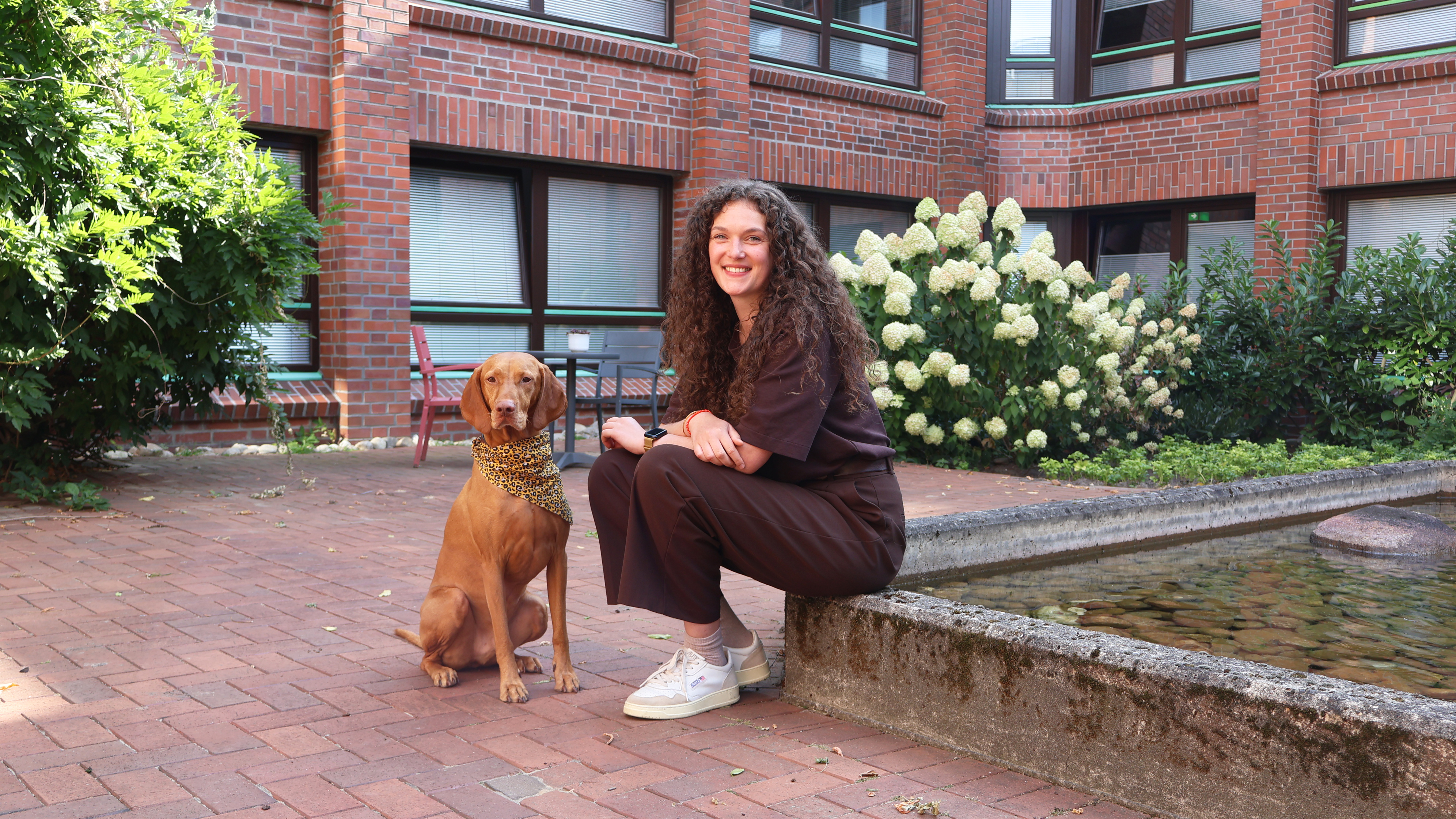 Gaby Beckmann, Mitarbeiterin im Internat des Berufsbildungswerks, sitzt gemeinsam mit ihrem Hund Carlo im Innenhof des Internats.