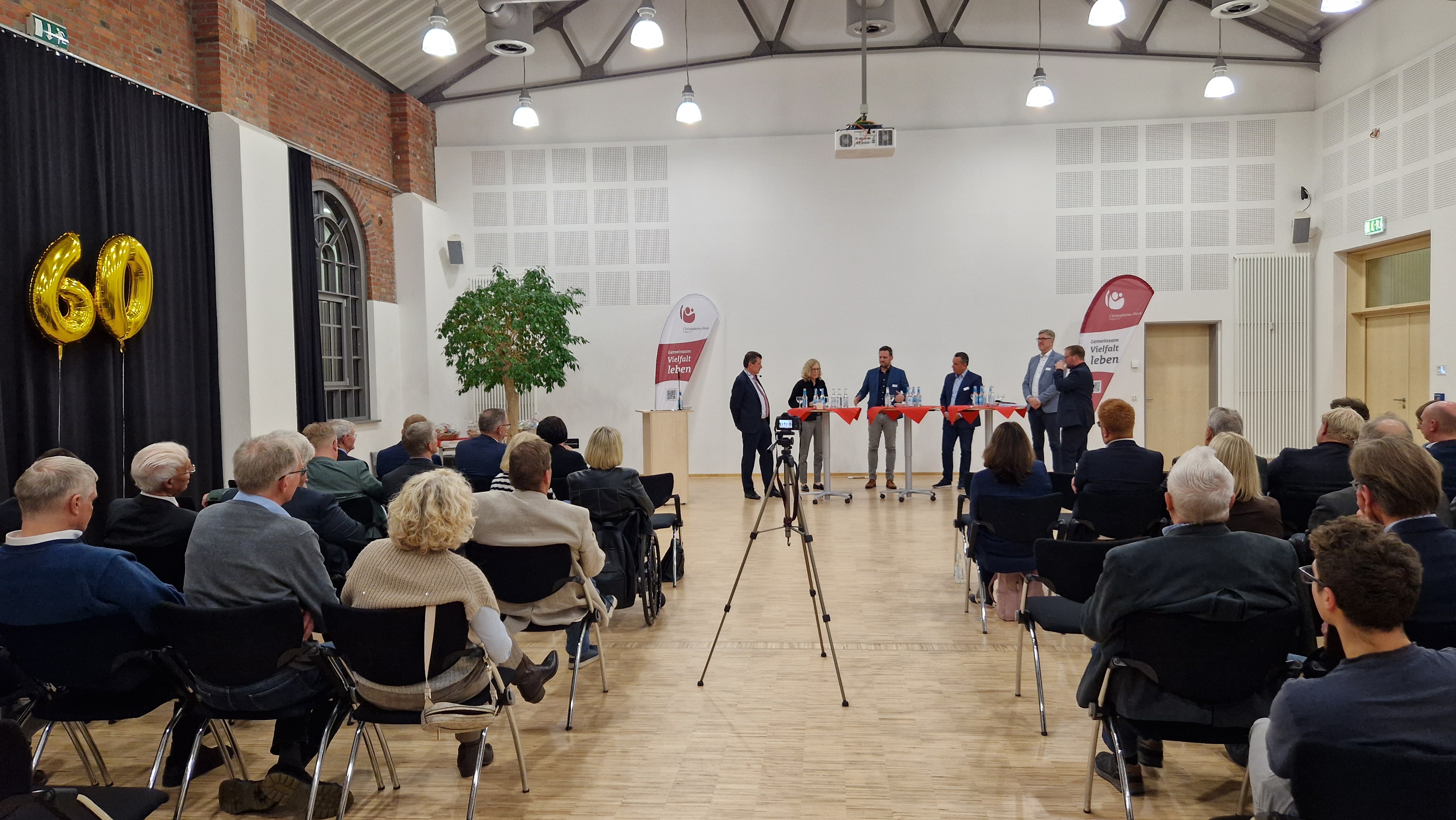 Ein großer Veranstaltungsraum mit besetzten Stuhlreihen und Menschen an Stehtischen, die miteinander reden.