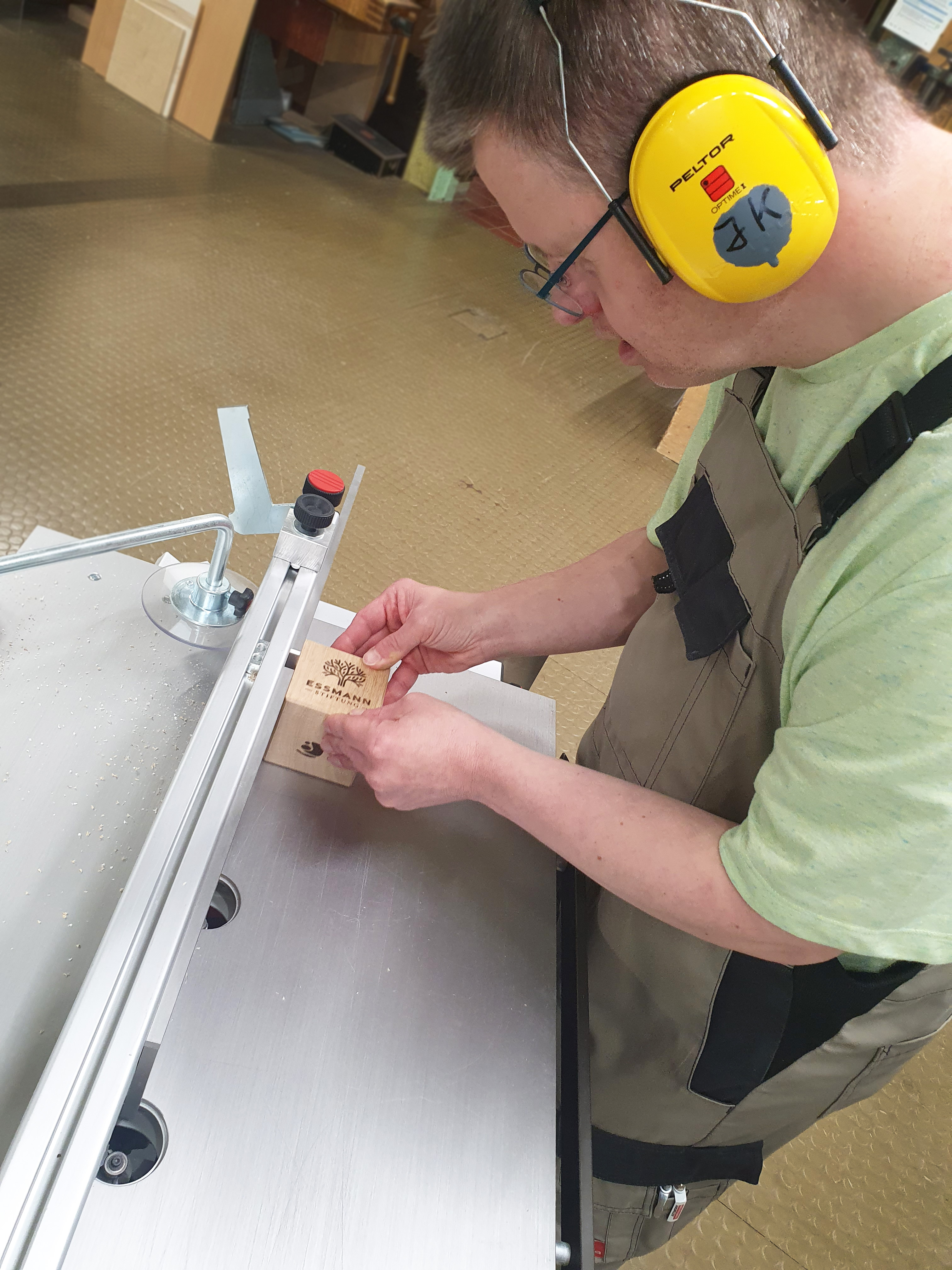 Ein Mann trägt Gehörschutz und arbeitet an einer Maschine in der Holzwerkstatt. Er glättet sorgfältig die Kanten des Pokals „Lingener Feder 2025“.