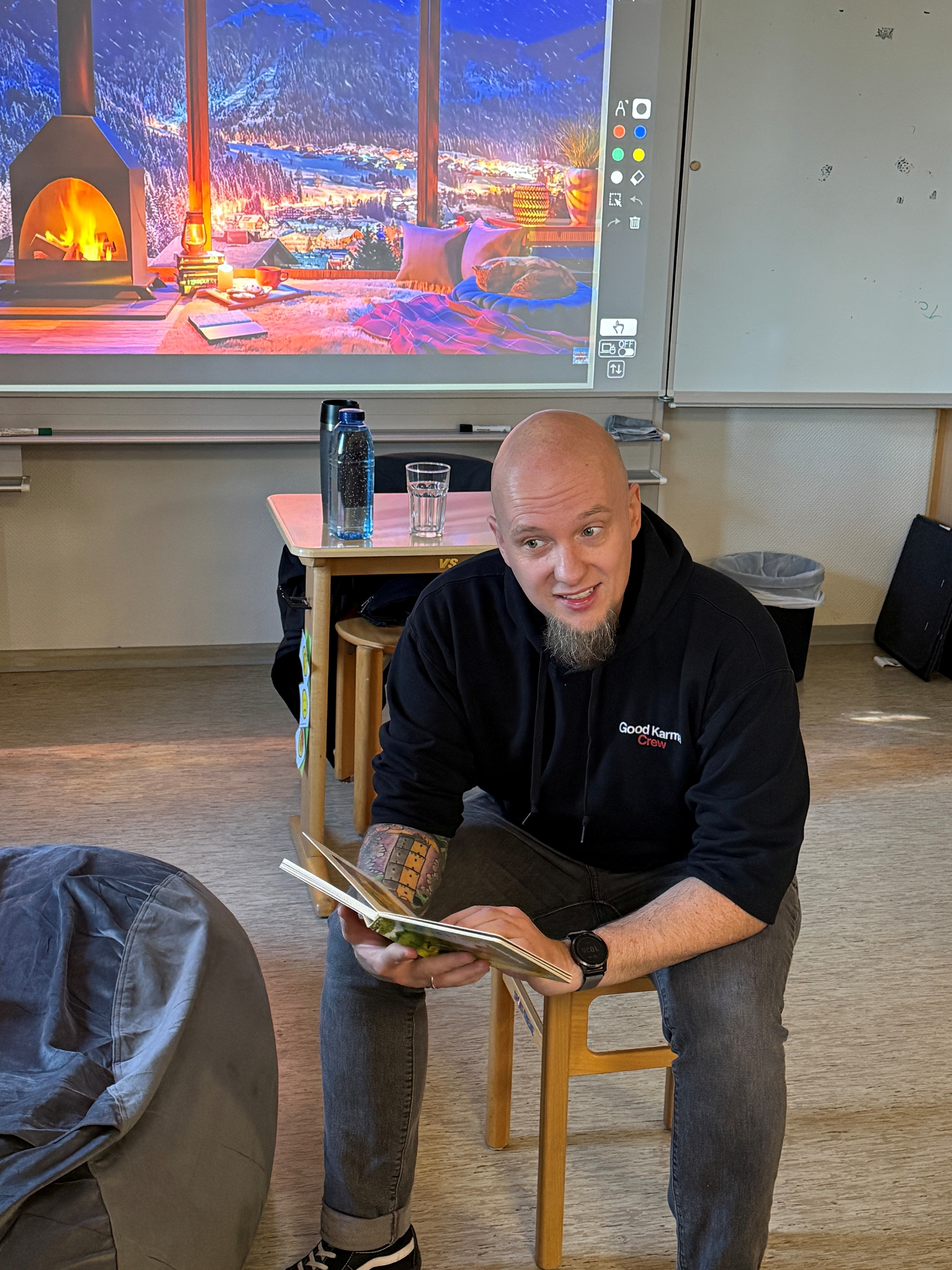 Ein Mann sitzt in einem Klassenraum und liest aus einem Buch vor