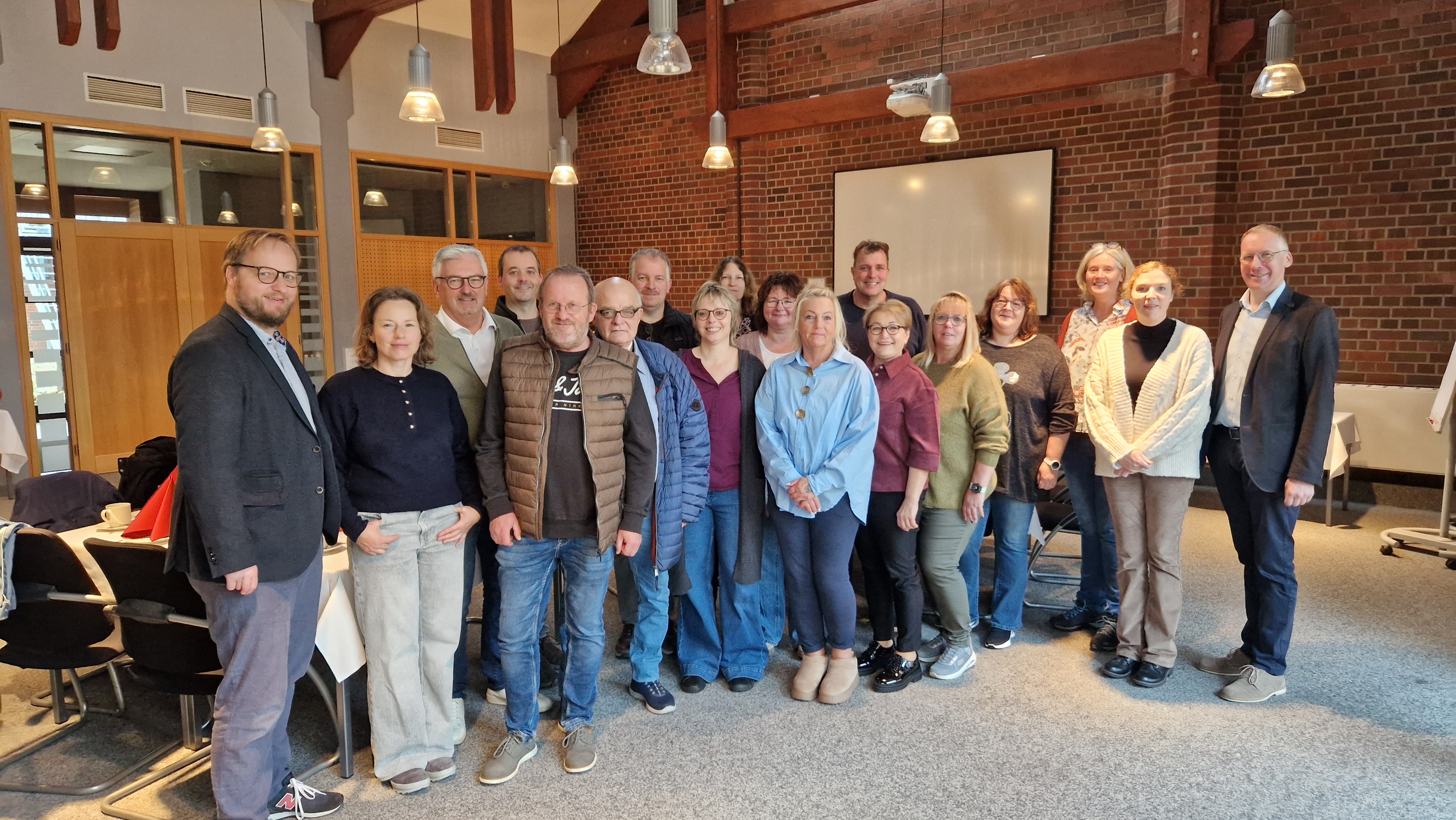 Eine Gruppe von 18 Personen posieren in einem Raum für ein Foto.