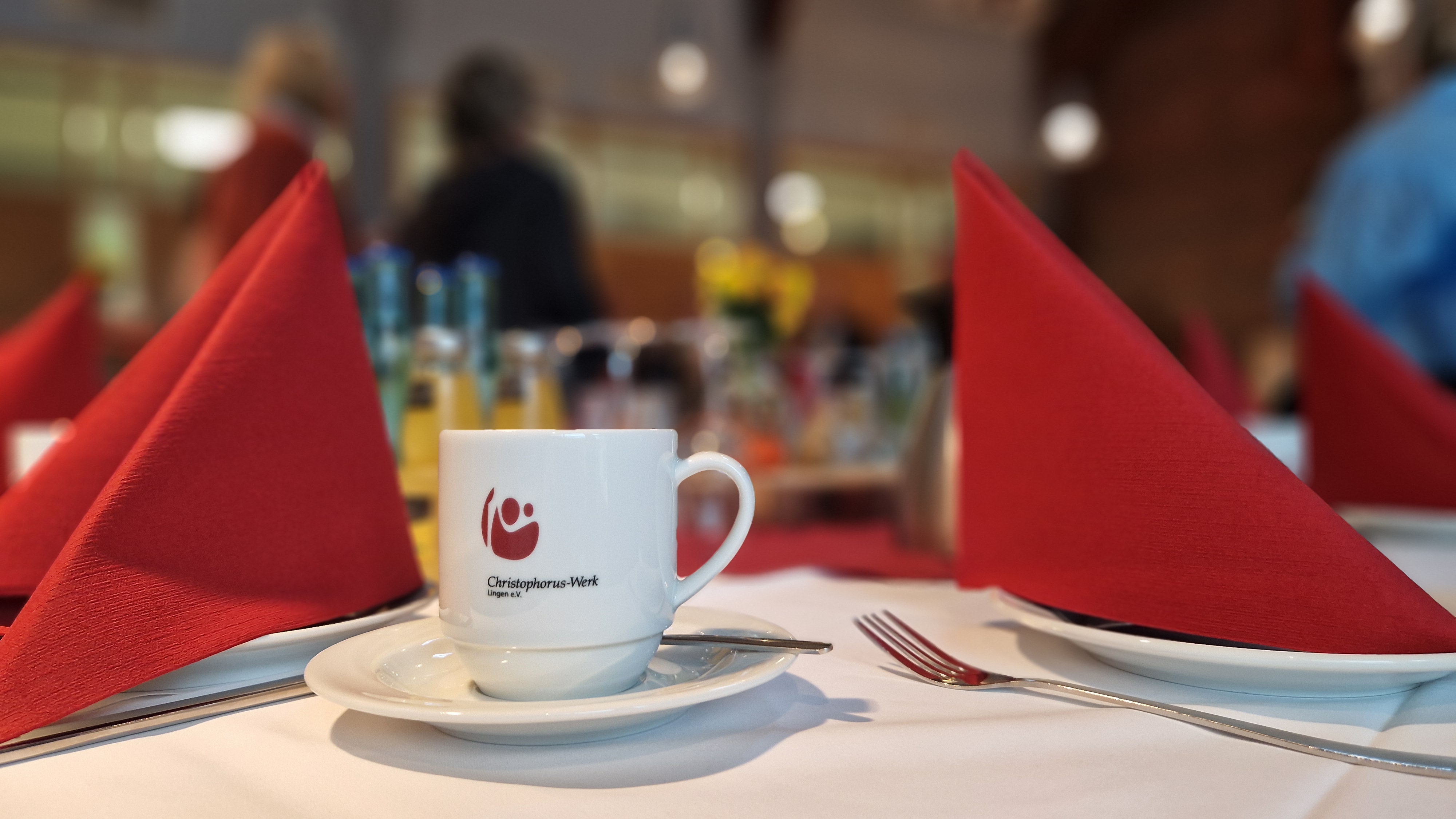 Ein Becher mit dem Logo des Christophorus-Werkes steht auf einem gedeckten Tisch.