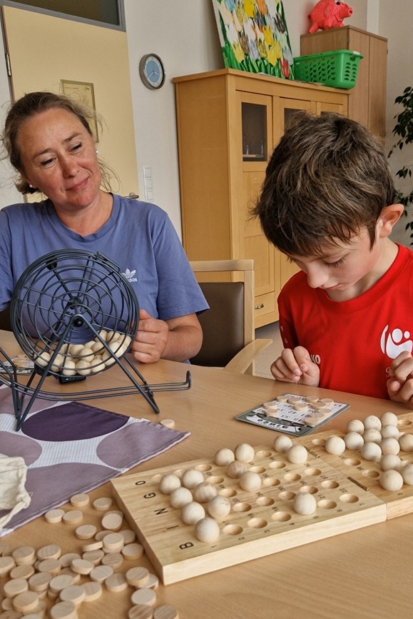 Eine Betreuungsperson sitzt gemeinsam mit einem Jungen an einem Tisch und begleitet ihn bei einem Gesellschaftsspiel mit Holzsteinen. Beide sind konzentriert und im Austausch.