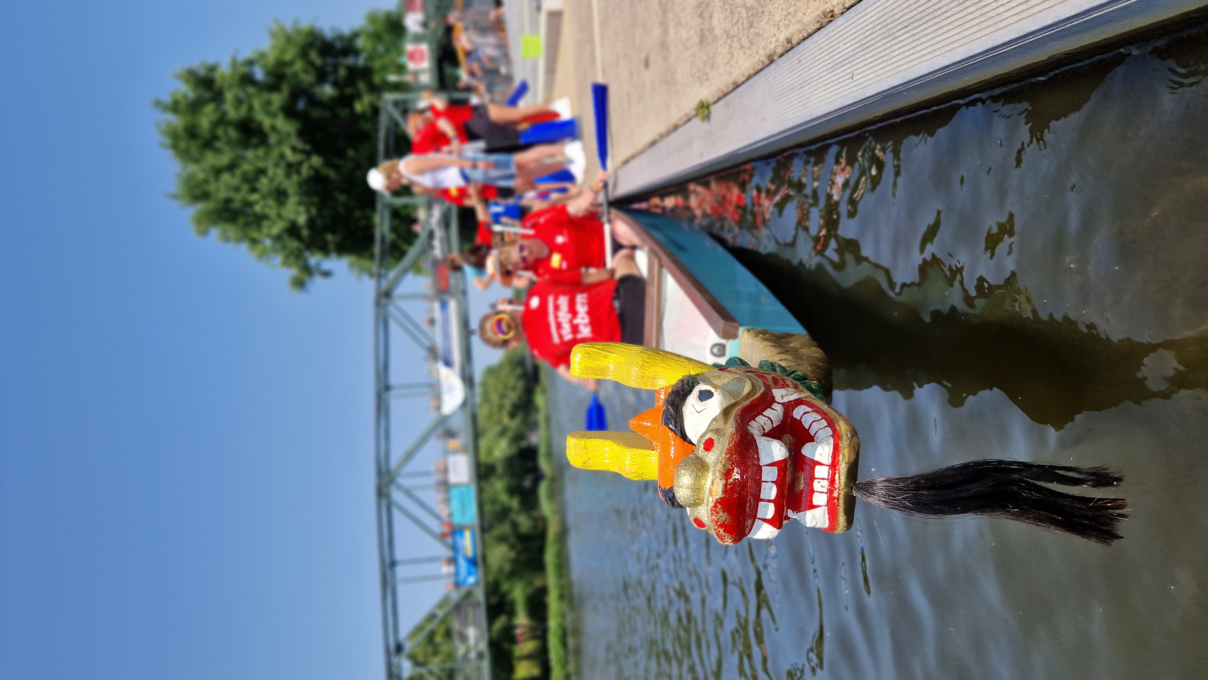 Drachenboot mit traditionellem buntem Drachenkopf am Steg. Im Hintergrund steigen Teammitglieder des Christophorus-Werks ins Boot ein – bereit für das nächste Rennen.