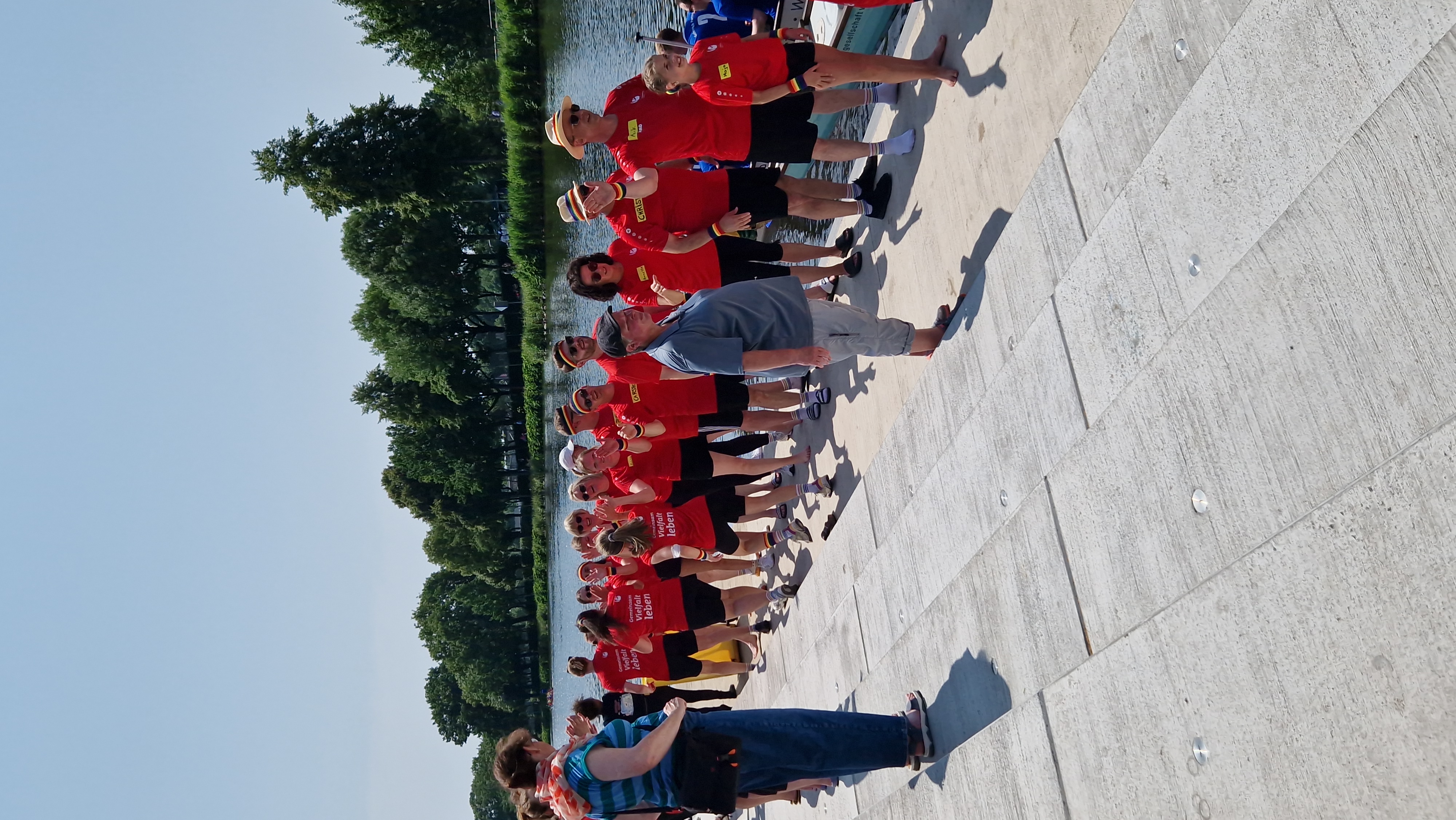 Das Christophorus-Team geht in einer langen Reihe barfuß und in roten Shirts am Wasser entlang – begleitet von Applaus und sommerlichem Wetter. 