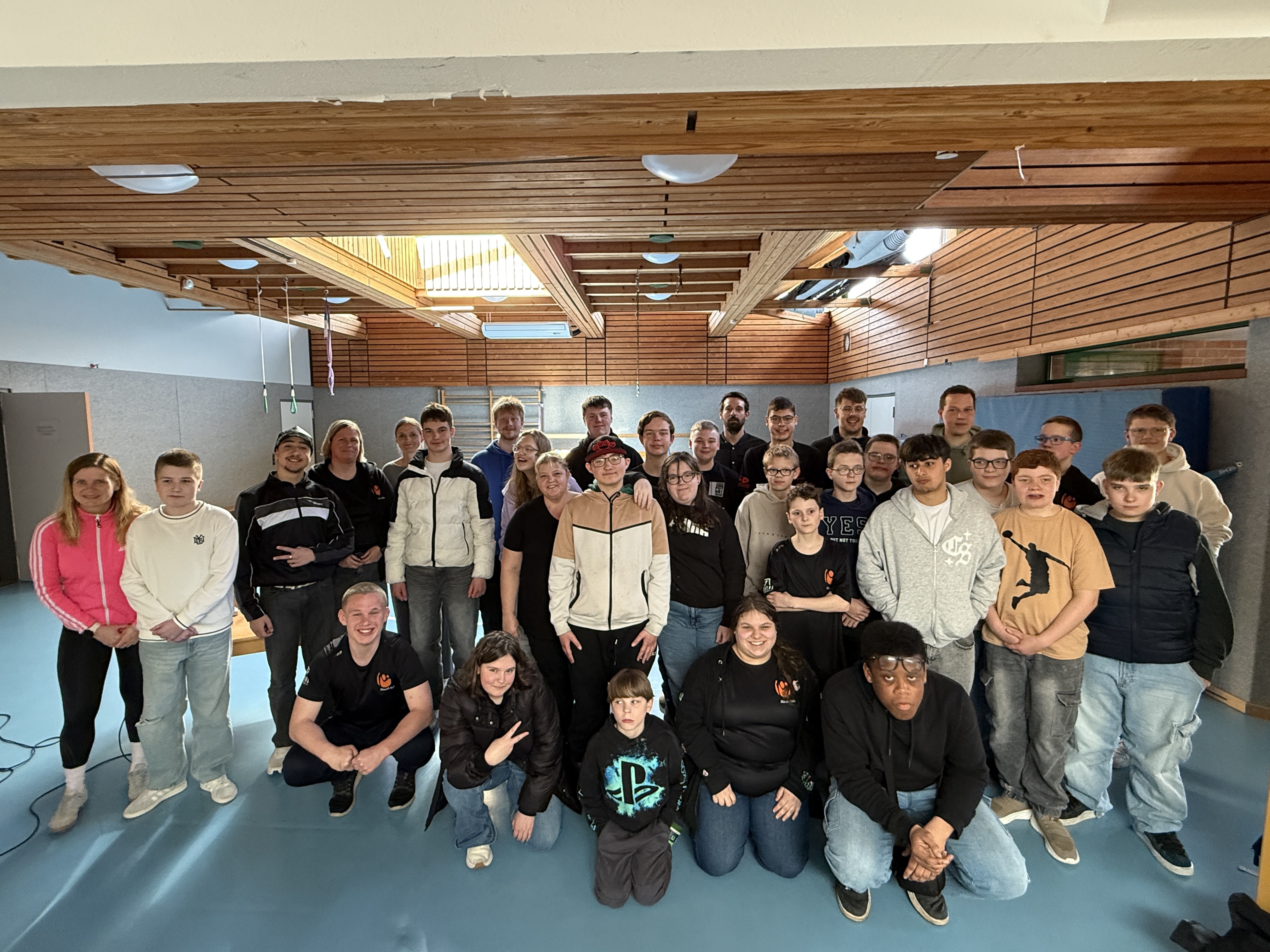 Es ist ein Gruppenfoto mit Sch&uuml;lerinnen und Sch&uuml;ler sowie Begleitpersonen in einem Innen-raum zu sehen. 