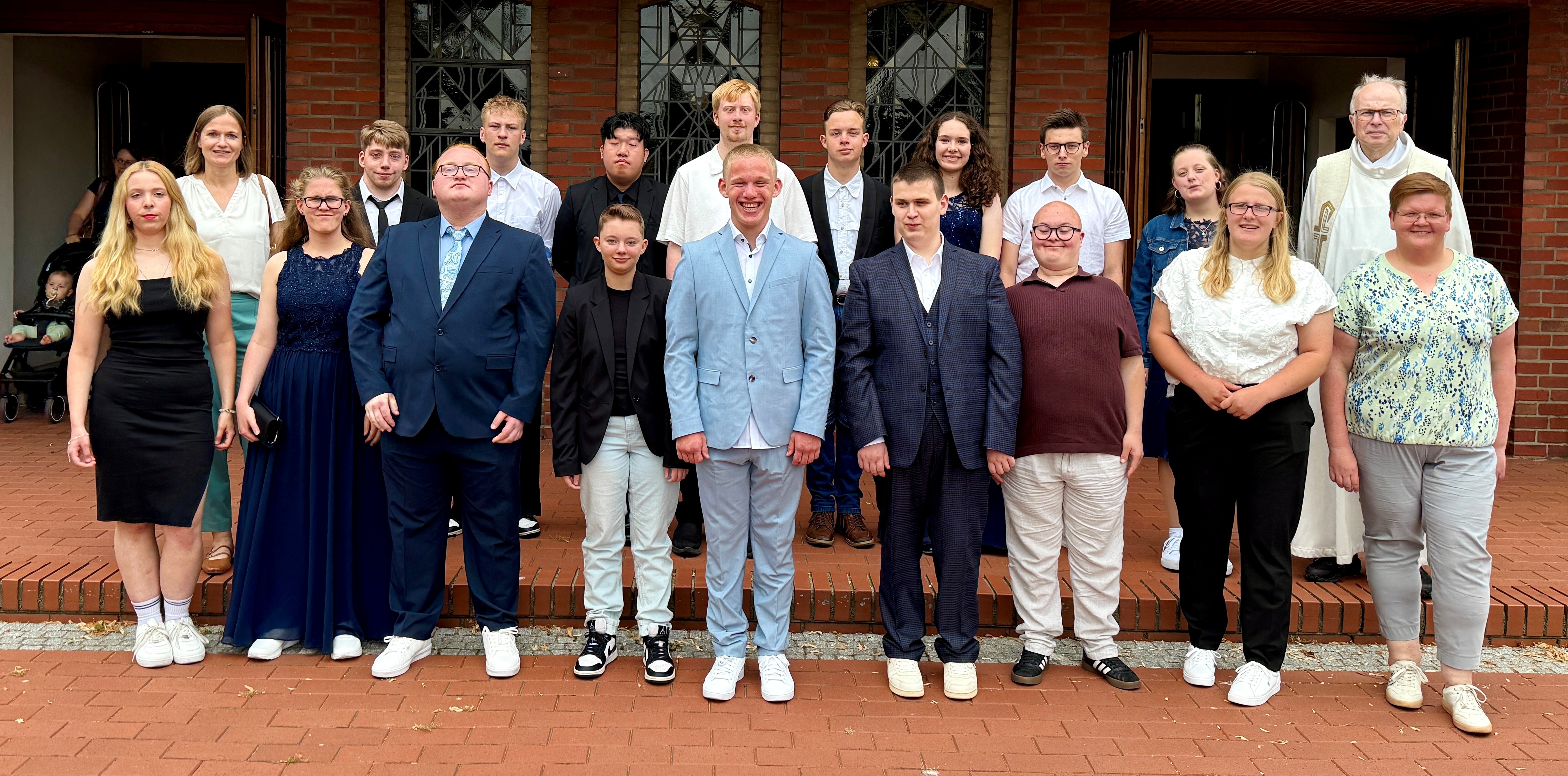 eine Gruppe von jungen Menschen steht vor einem Geb&auml;ude. In der hinteren Reihe steht ein Geistlicher, vor ihm eine etwas &auml;ltere Frau.