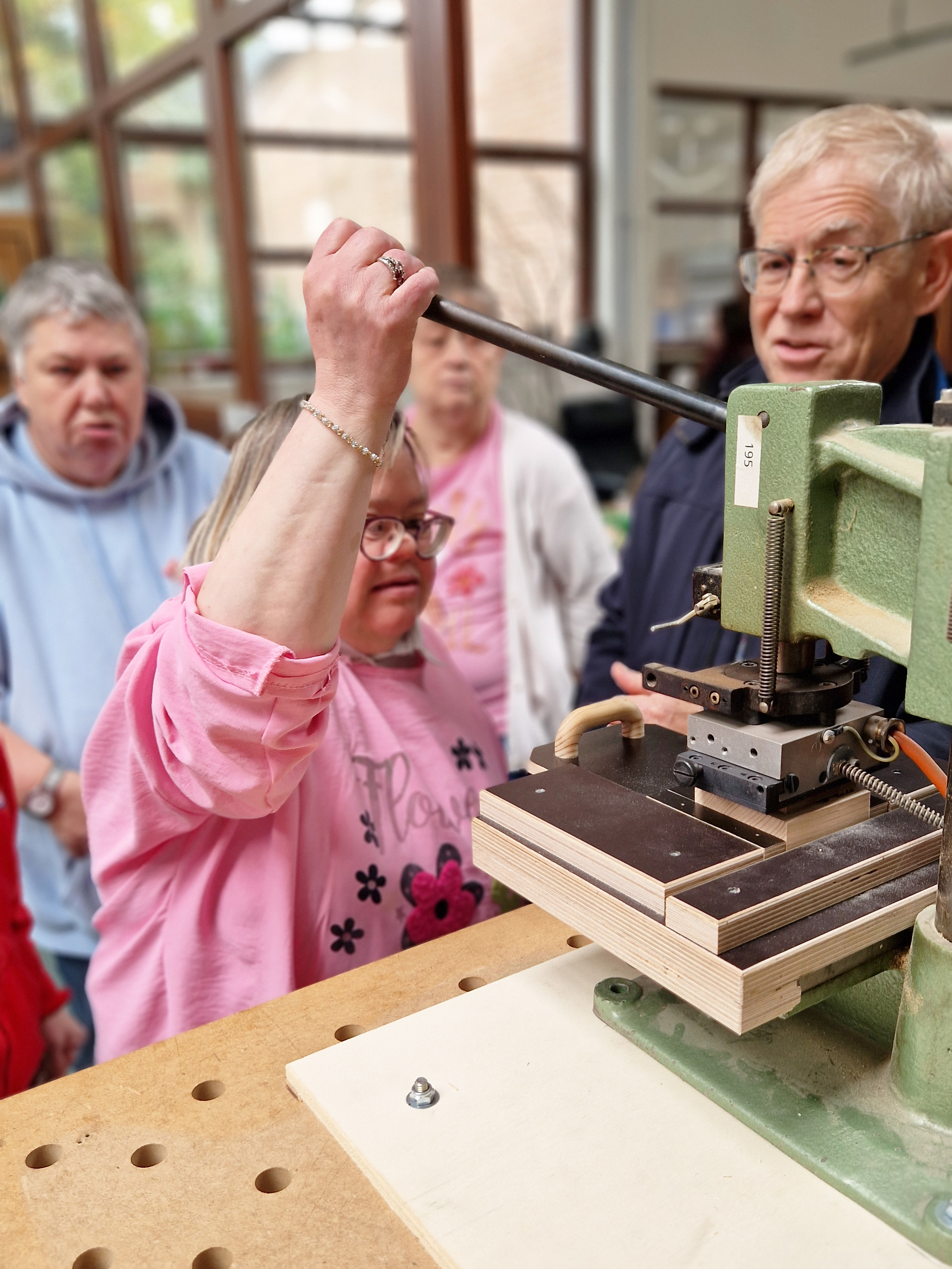 Drei Frauen stehen hinter einer Maschine. Die eine drückt einen Hebel der Maschine nach unten. Ein Mann steht daneben und spricht zu den Frauen. 