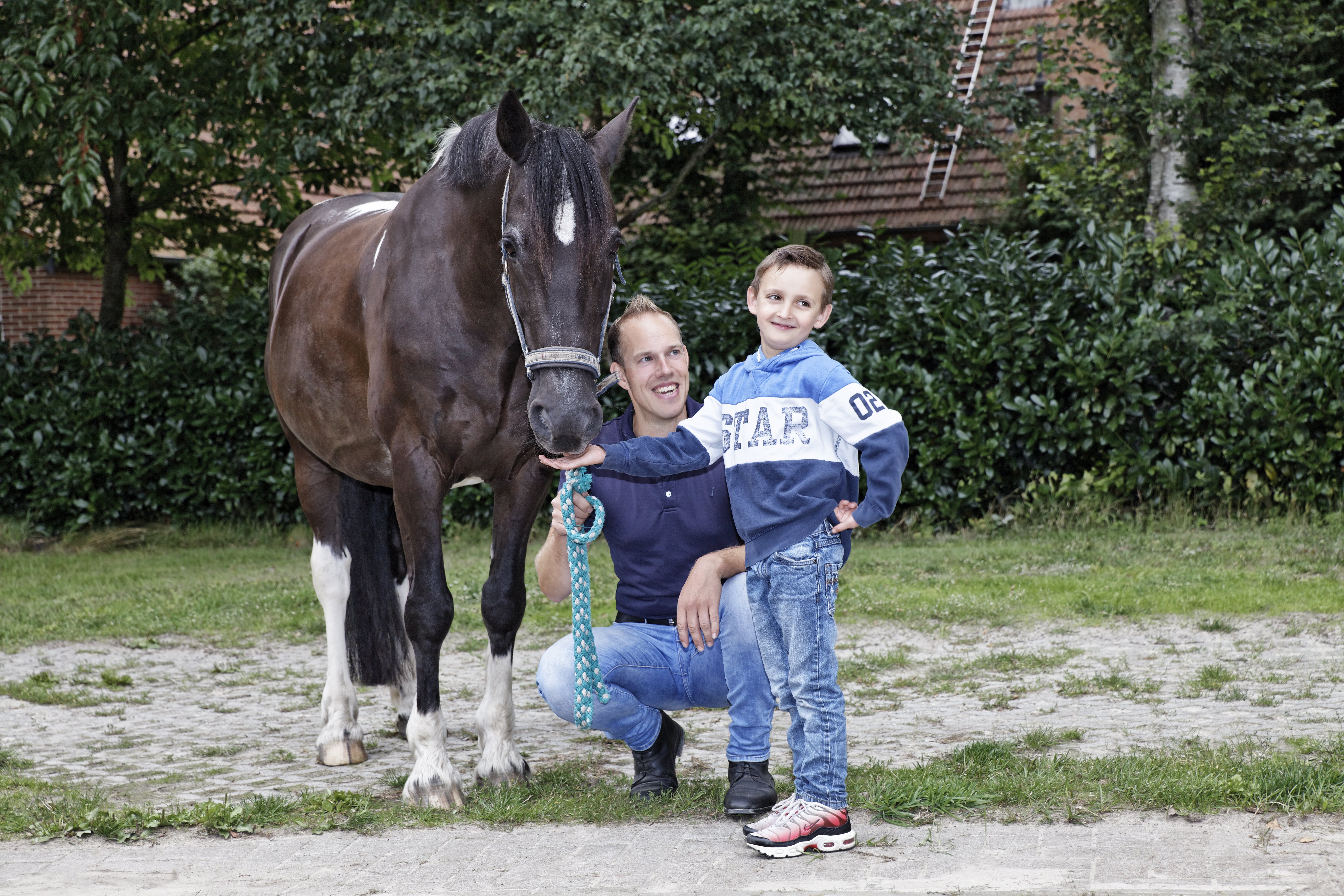 Reittherapeut Michael Menger steht gemeinsam mit einem Klient und einem Pferd in der Weide.