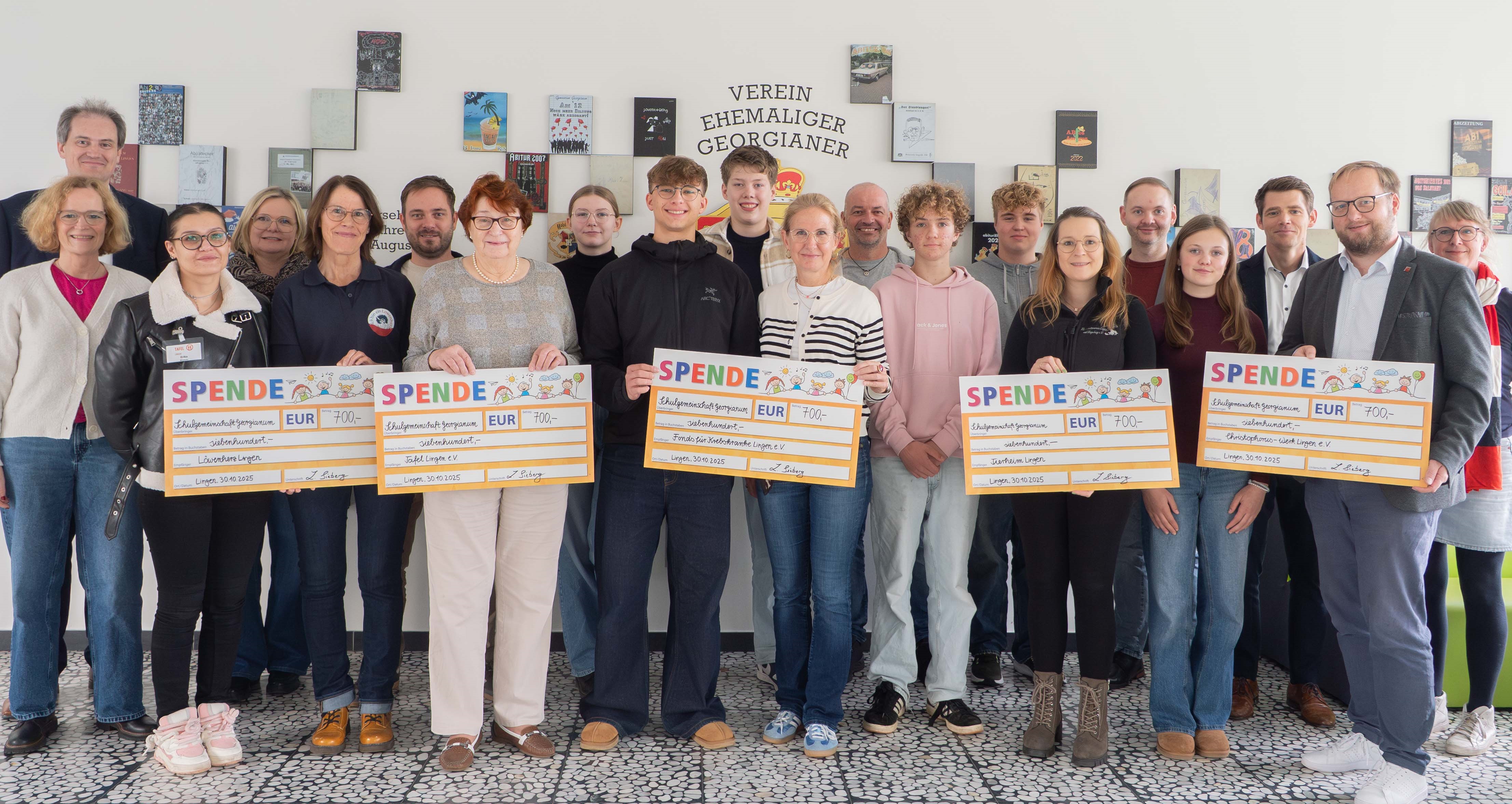 Eine große Gruppe Menschen schaut lächelnd in die Kamera. Fünf Personen halten jeweils einen großen Scheck in der Hand.