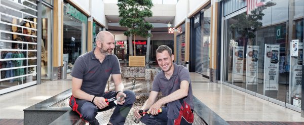 Teilnehmer und sein Anleiter reinigen einen Brunnen in einer Einkaufspassage.