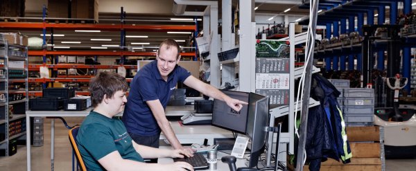 Anleiter zeigt Auszubildendem etwas auf dem PC im Lager.