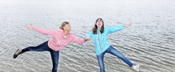 Betreuerin und Klienten stehen am Ufer eines Sees auf einem Bein.