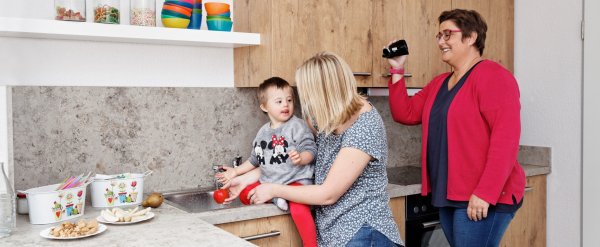 Mutter mit ihrem Kind in der Küche. Eine Mitarbeiterin filmt die beiden mit einer Kamera.