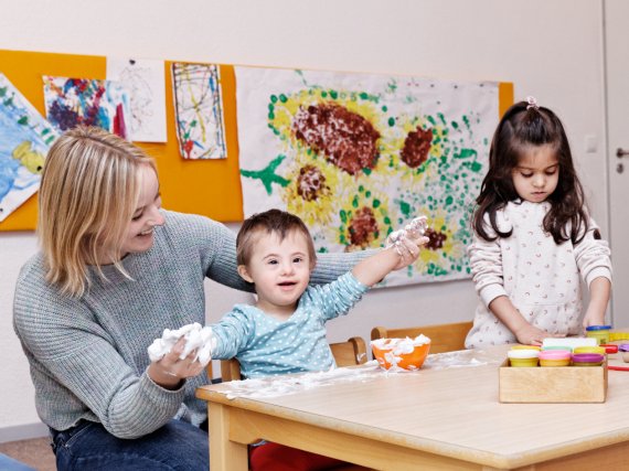 Mitarbeiterin betreut zwei Kinder beim Spielen am Basteltisch.