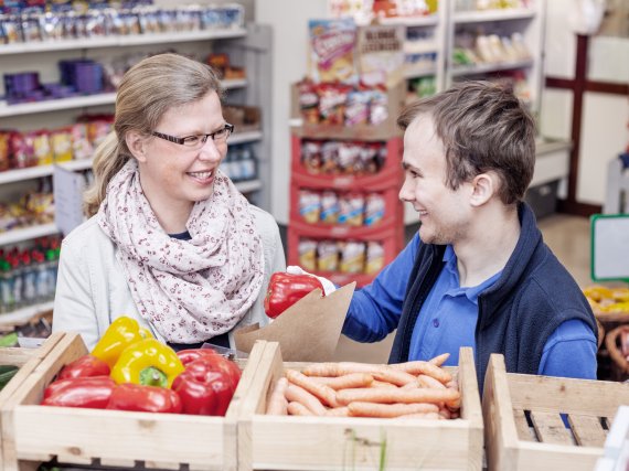 Kauffrau im Einzelhandel und Beschäftigter im Laden hinter Gemüsekisten.