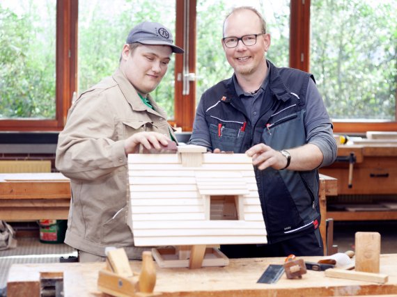 Tischler und Beschäftigter schmirgeln Vogelhaus in Holzwerkstatt.