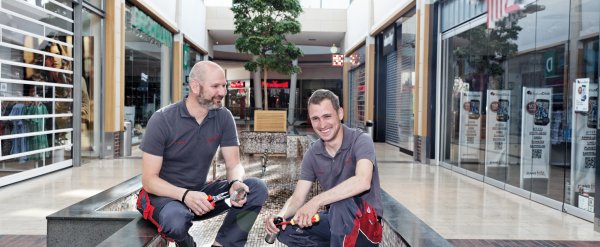 Teilnehmer und sein Anleiter reinigen einen Brunnen in einer Einkaufspassage.