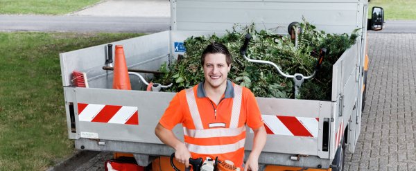 Teilnehmer steht mit elektrischer Heckenschere vor einer Ladefläche mit Grünabfall.