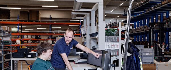 Anleiter zeigt Auszubildendem etwas auf dem PC im Lager.