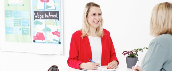 Fachkraft und Teilnehmerin im Gespräch an einem Stehtisch.