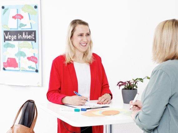 Fachkraft und Teilnehmerin im Gespräch am Stehtisch.