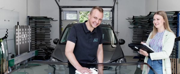 TeilnehTeilnehmer poliert eine Autoscheibe, Fachkraft steht mit Notizheft daneben.