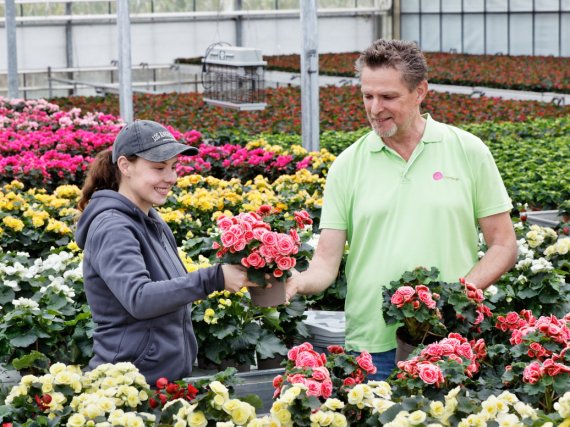Auszubildende mit Anleiter in einer Gewächshalle inmitten von Blumen.