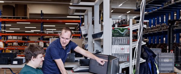 Anleiter zeigt Auszubildendem etwas auf dem PC im Lager.