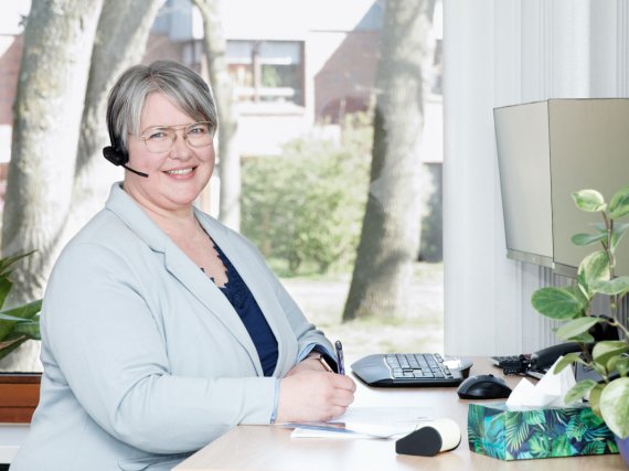 Mitarbeiterin hat Headset am Ohr und steht am Schreibtisch.