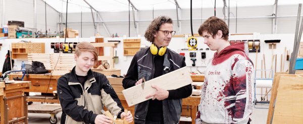Anleiter und zwei Auszubildende in der Holzwerkstatt.