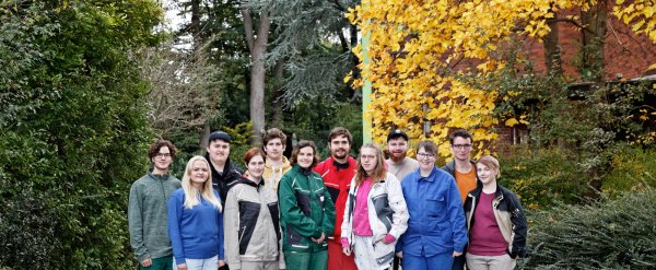 Eine Gruppe von Auszubildenden in verschiedener Arbeitskleidung steht vor Hecken und Sträuchern.