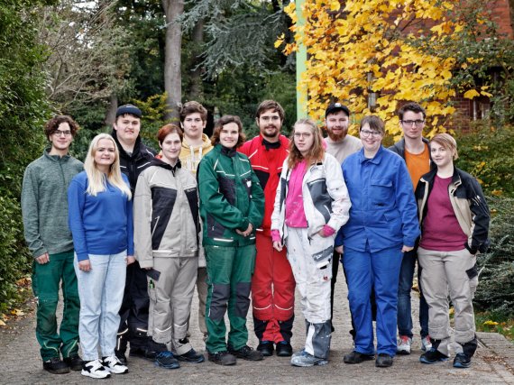 Eine Gruppe von Auszubildenden in verschiedener Arbeitskleidung steht vor Hecken und Sträuchern.