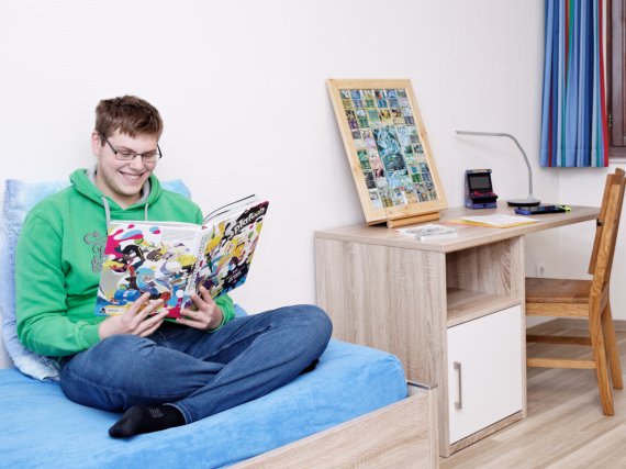 Auszubildender sitzt in seinem Zimmer auf dem Bett und liest ein Buch.