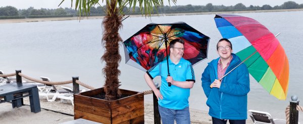Zwei Männer mit bunten Schirmen am Strand.