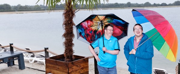 Zwei Männer mit bunten Schirmen am Strand.