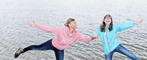 Betreuerin und Klienten stehen am Ufer eines Sees auf einem Bein.