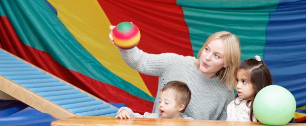 Mitarbeiterin und zwei Kinder spielen in einer Turnhalle mit zwei Bällen.