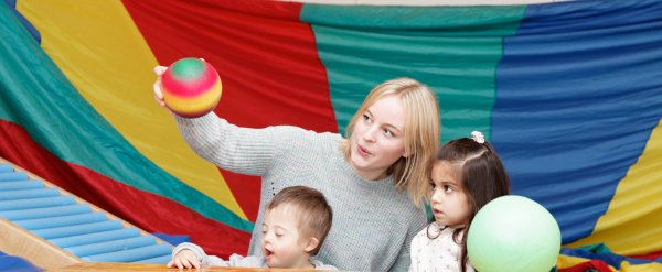 Mitarbeiterin und zwei Kinder spielen in einer Turnhalle mit zwei Bällen.