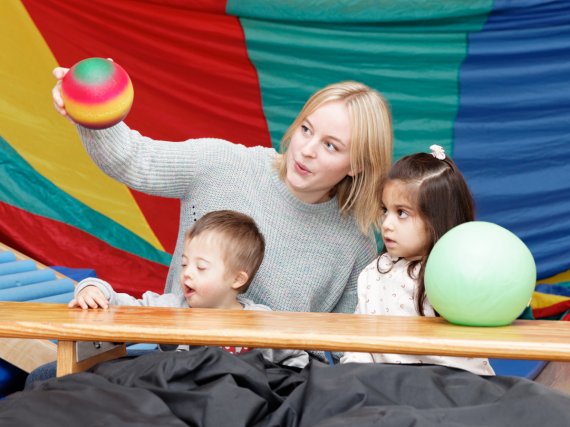 Mitarbeiterin und zwei Kinder spielen in einer Turnhalle mit zwei Bällen.
