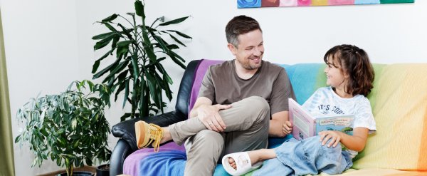 Betreuer und Kind lesen Buch auf dem Sofa.