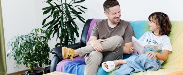 Betreuer und Kind lesen Buch auf dem Sofa.